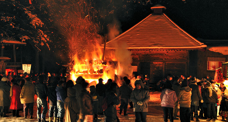 燃え上がる歳戸木の火に浮かび上がる熊野神社本殿。