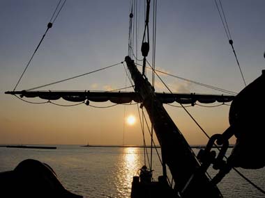 船首甲板部から見た折りたたまれた帆と夕日。